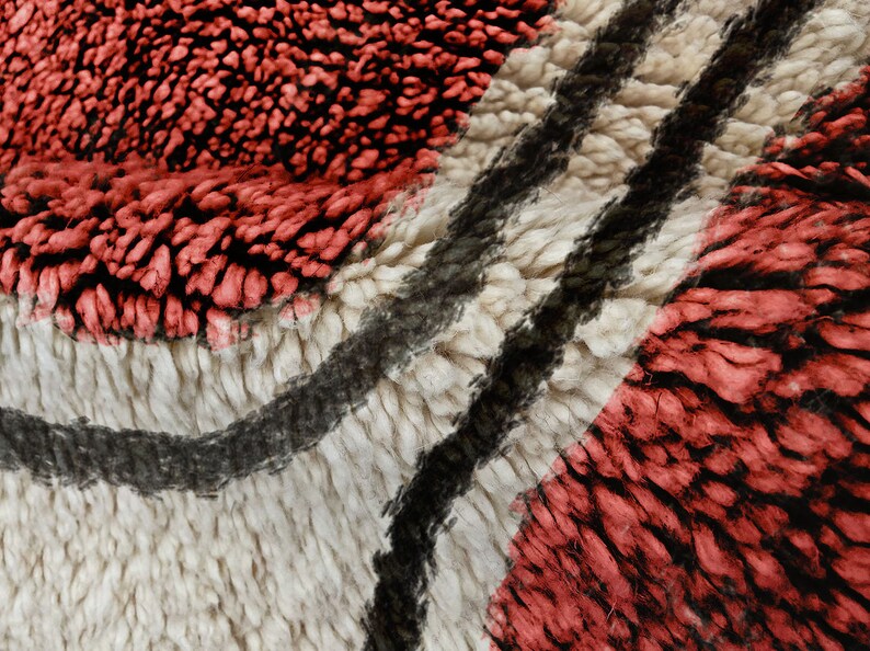 May include: A thick, high-pile rug featuring a textured pattern of deep red, cream, and black fibres. The surface displays a dense, shaggy weave with undulating dark lines that contrast against the lighter cream and vibrant red sections.