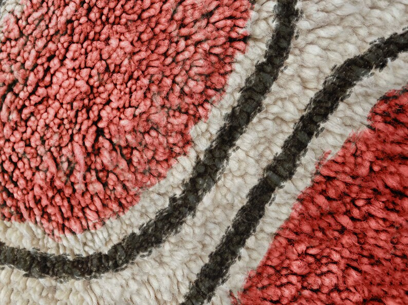May include: A close-up view of a textured rug featuring thick, looped pile in shades of coral pink and cream, separated by two distinct, curved dark charcoal grey lines that create a flowing, organic pattern across the surface.