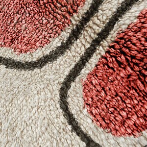May include: A thick, high-pile rug featuring a cream-coloured background with large, rounded, coral-pink tufted shapes outlined by dark charcoal-grey lines. The texture is dense and shaggy, creating a soft, tactile surface with distinct colour blocks.