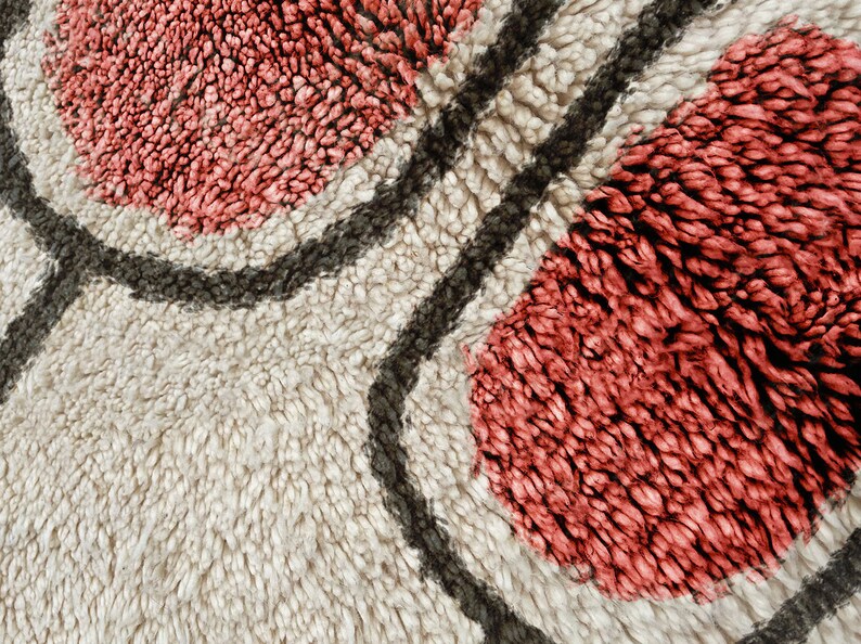 May include: A thick, high-pile rug featuring a cream-coloured background with large, rounded, coral-pink tufted shapes outlined by dark charcoal-grey lines. The texture is dense and shaggy, creating a soft, tactile surface with distinct colour blocks.