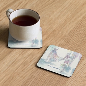 May include: Square coasters with a fashion illustration design. One coaster has a white mug with tea on it. The other coaster has a fashion illustration of a dress and suit. The text "CODE FASHIONABLY" is printed on the bottom of each coaster.