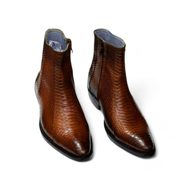 May include: Two brown leather ankle boots with a snakeskin texture. Each boot features a side zip and a rounded toe. The interior lining is light blue. The boots are displayed on a white background. The boots are a stylish footwear option.