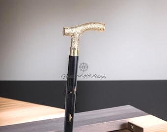 Könnte beinhalten: Schwarzer Gehstock mit goldfarbenem Griff und Akzenten. Der Griff hat ein verziertes Blumenmuster. Der Stock besteht aus Holz und Metall. Der Stock ist etwa 91 cm lang.
