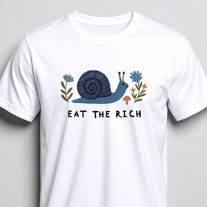 Könnte beinhalten: Weißes T-Shirt mit einem blauen Schnecken-Design und dem Text "EAT THE RICH". Die Schnecke ist von blauen Blumen und einem kleinen orangefarbenen Pilz umgeben. Der Aufdruck befindet sich auf der Vorderseite des T-Shirts.