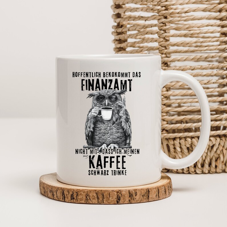 Puede incluir: Taza de caf&eacute; de cer&aacute;mica blanca con una ilustraci&oacute;n en blanco y negro de un b&uacute;ho sosteniendo una taza de caf&eacute;. La taza tiene texto en alem&aacute;n: "Espero que a la oficina de impuestos no le importe que beba mi caf&eacute; solo."