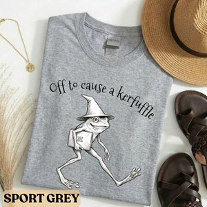 Könnte beinhalten: Eine weiße Keramik-Tasse mit schwarzem Henkel und dem Text "But First, Coffee" in fetter, schwarzer Schrift. Die Tasse steht vor einem verschwommenen Hintergrund. Die Tasse ist etwa 10 cm hoch.