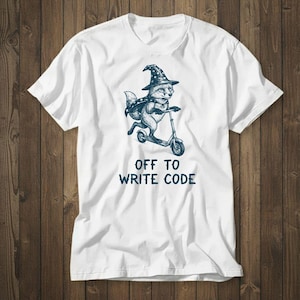 Könnte beinhalten: Weißes T-Shirt mit einer marineblauen Illustration eines Fuchses mit Zaubererhut und Umhang, der Roller fährt. Der Text "OFF TO WRITE CODE" ist darunter in Marineblau gedruckt.
