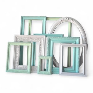 May include: A collection of decorative picture frames in various sizes and shapes. The frames are painted in shades of teal, silver, and pale green. Some frames have ornate detailing, while others are simple. The frames are arranged against a white background.