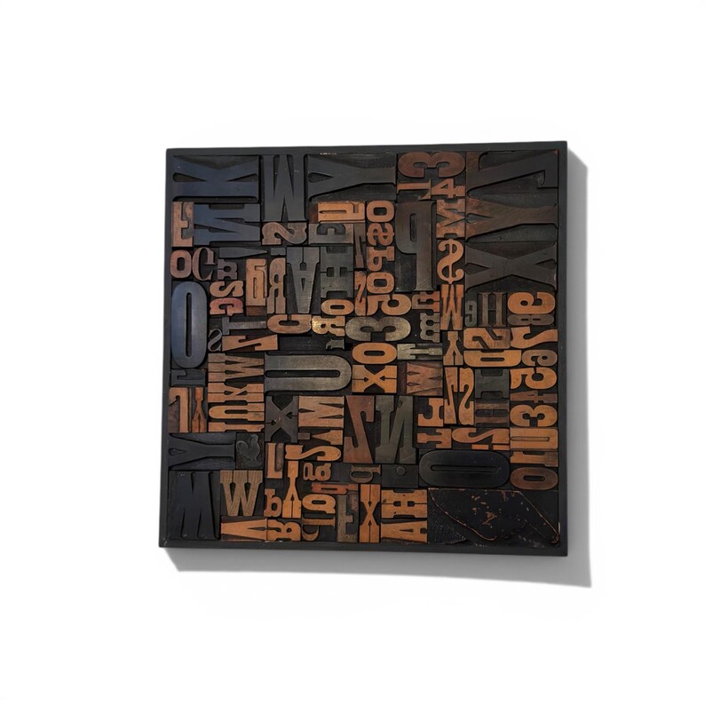 May include: A square, wooden block filled with various vintage letterpress printing blocks. The letters and numbers are in a mix of sizes and fonts, with a dark brown and orange color scheme. The block is set against a white background.