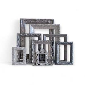May include: A collection of ornate, silver-toned picture frames of various sizes and shapes. The frames have detailed, textured designs and are arranged against a white background. The frames are empty, ready for photos or artwork.
