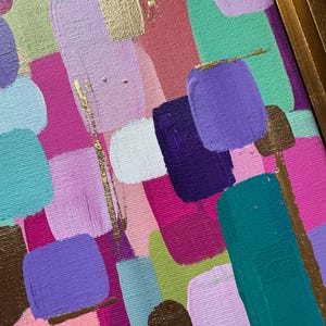 Peut inclure: Peinture abstraite encadr&eacute;e d'or. L'&oelig;uvre pr&eacute;sente une composition color&eacute;e de coups de pinceau dans les tons de rose, de violet, de turquoise et d'or. La peinture a un aspect textur&eacute;, avec des marques de pinceau visibles et un cadre dor&eacute;.