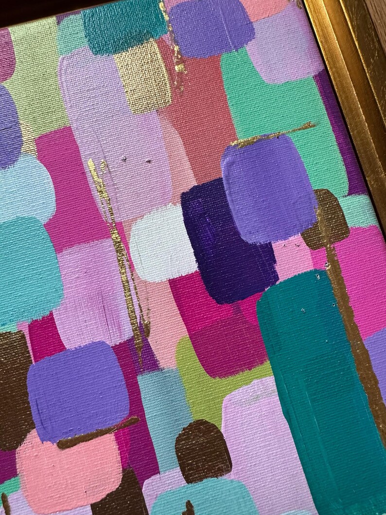 Peut inclure: Peinture abstraite encadr&eacute;e d'or. L'&oelig;uvre pr&eacute;sente une composition color&eacute;e de coups de pinceau dans les tons de rose, de violet, de turquoise et d'or. La peinture a un aspect textur&eacute;, avec des marques de pinceau visibles et un cadre dor&eacute;.