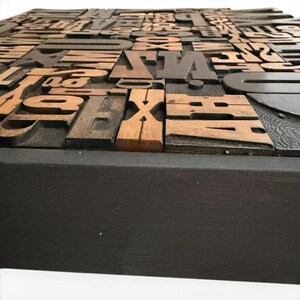 May include: A collection of vintage wooden letterpress printing blocks, featuring various fonts and sizes. The blocks are arranged on a dark wooden base, showcasing the natural wood grain and the aged appearance of the printing tools.