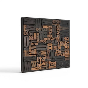 May include: A square, wooden block filled with various wooden letterpress printing blocks. The letters and numbers are in a mix of sizes and fonts, with a dark brown and natural wood color scheme. The block is set against a white background.