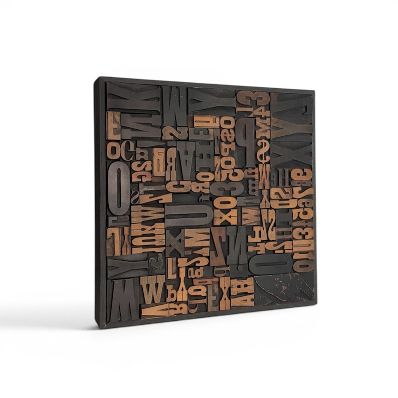 May include: A square, wooden block filled with various wooden letterpress printing blocks. The letters and numbers are in a mix of sizes and fonts, with a dark brown and natural wood color scheme. The block is set against a white background.
