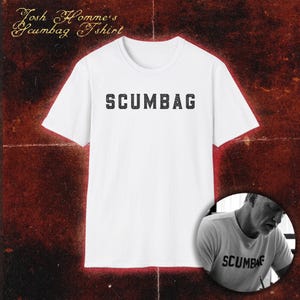 Può includere: Una t-shirt bianca a maniche corte con la parola SCUMBAG stampata in un carattere nero, usurato e in stampatello sul petto. Il testo Josh Homme's Scumbag Tshirt appare in alto a sinistra e un inserto circolare mostra la t-shirt indossata.