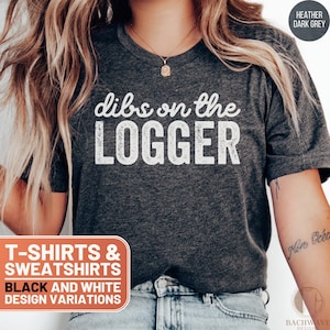 May include: A heather dark grey t-shirt with the text "dibs on the LOGGER" in white. The text has a distressed, vintage look. The t-shirt is available in black and white design variations.