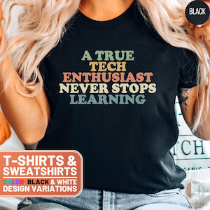 May include: A black t-shirt with the text "A True Tech Enthusiast Never Stops Learning" in a retro font with colorful accents. The text is centered on the shirt. T-shirts and sweatshirts are available in black and white.