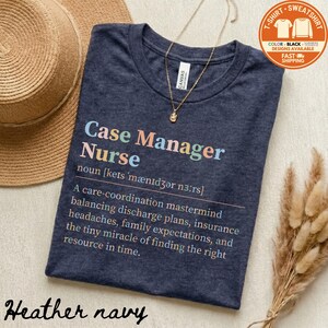 May include: Heather navy t-shirt with the text "Case Manager Nurse" in colorful letters. The shirt includes a definition of the term. A gold necklace and a straw hat are also in the image.
