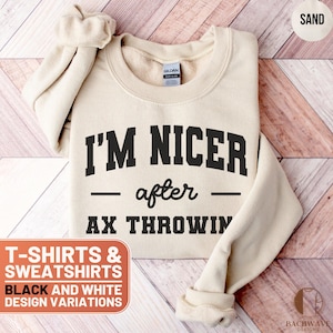 May include: A beige sweatshirt with black text that reads "I'm Nicer - after - AX Throwin". The sweatshirt is on a wooden surface. T-shirts and sweatshirts are available in black and white design variations.