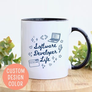 May include: White ceramic mug with a black interior and handle. The mug features the text "Software Developer Life" in a handwritten font, along with illustrations of a laptop, code brackets, and a lightning bolt. A peach-colored circle with the text "CUSTOM DESIGN COLOR" is on the bottom left.