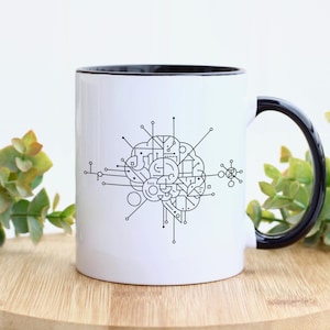 May include: White ceramic mug with a black interior and handle. The mug features a black and white geometric design resembling a brain. The mug is sitting on a wooden surface.