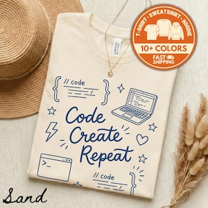 May include: A sand-colored t-shirt with the words "Code Create Repeat" in navy blue, along with related graphics like a laptop and code symbols. The shirt also features the text "10+ COLORS" and "FAST SHIPPING" in a circular orange graphic.
