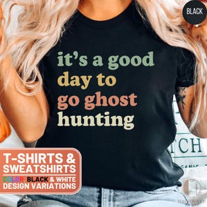 May include: Black t-shirt with the text "it's a good day to go ghost hunting" in a retro font with colorful accents. The text is centered on the shirt. T-shirts and sweatshirts are available in black and white.