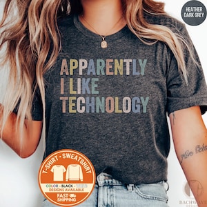 May include: Dark gray t-shirt with the text "APPARENTLY I LIKE TECHNOLOGY" in colorful, block letters. The shirt has a crew neck and short sleeves. Additional text on the shirt includes "T-SHIRT SWEATSHIRT" and "COLOR - BLACK - WHITE DESIGNS AVAILABLE FAST SHIPPING".