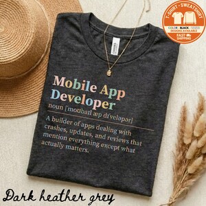 May include: Dark heather grey t-shirt with the text "Mobile App Developer" in colorful letters. The shirt includes a definition of the term. A gold necklace and a straw hat are also visible.