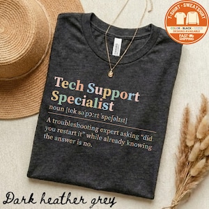 May include: Dark heather grey t-shirt with the text "Tech Support Specialist" in colorful letters. The shirt includes a definition and a humorous quote about troubleshooting. A gold necklace with a pendant is on the shirt.