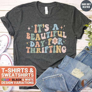 May include: A dark grey heather t-shirt with the text "It's a beautiful day for thrifting" in colorful retro font. The text is surrounded by small stars and a smiley face flower.