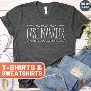 May include: A dark grey heather t-shirt with the text "I'm a Case Manager, what's your superpower?" printed in white. The t-shirt is displayed on a white wooden surface with a pair of white sneakers and blue jeans.