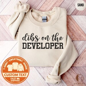 May include: A white ceramic mug with a black handle and the text "But First, Coffee" in a bold, black font. The mug is set against a blurred background, suggesting a cozy setting. The mug appears to be approximately 4 inches tall.