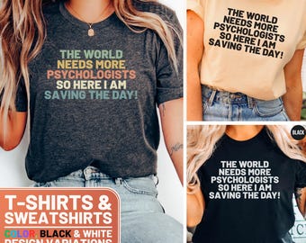 May include: Three t-shirts with the text "The world needs more psychologists so here I am saving the day!" in black and white. The shirts are shown in dark grey heather, cream, and black.