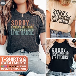 May include: Three t-shirts with the text "Sorry... I wasn't listening. I was thinking about line dance." in a vintage style font. The shirts are in dark grey heather, cream, and black.