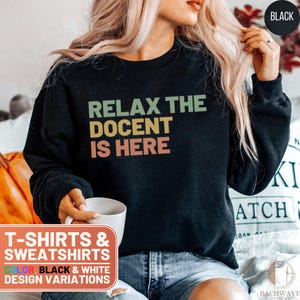 May include: Black sweatshirt with the text "Relax the Docent is Here" in a retro font with yellow, green, and orange colors.