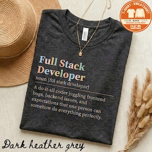 May include: Dark heather grey t-shirt with the text "Full Stack Developer" in colorful letters. The shirt includes a definition of the term. A gold necklace and a straw hat are also visible.