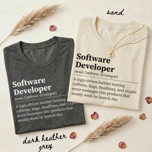 Two t-shirts, one dark heather grey, one sand, with text about a software developer.
