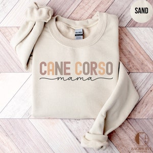 May include: A sand-colored sweatshirt with the text "CANE CORSO mama" in brown, peach, and pink lettering.