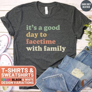 May include: A dark grey heather t-shirt with the text "it's a good day to facetime with family" in a retro rainbow color scheme. The shirt is available in black and white design variations.