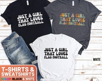May include: Three t-shirts with the text "Just a girl that loves flag football" in a retro font. The shirts are in black, white, and dark grey heather.
