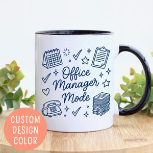May include: White ceramic mug with a black interior and handle. The mug features the text "Office Manager Mode" in navy blue script, surrounded by office-themed illustrations. A peach-colored circle with the text "CUSTOM DESIGN COLOR" is on the bottom left.