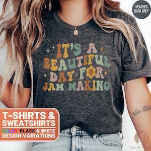 May include: A heather dark grey t-shirt with the text "It's a beautiful day for jam making" in colorful retro font. The text is surrounded by small stars and a smiley face flower.