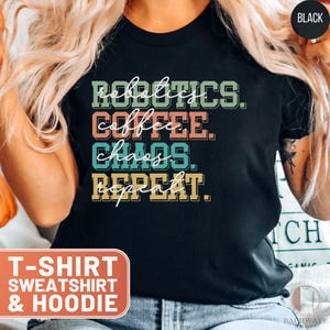 May include: Black t-shirt with the text "Robotics. Coffee. Chaos. Repeat." in colorful retro-style lettering.
