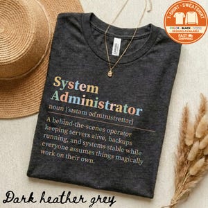 May include: Dark heather grey t-shirt with the definition of "System Administrator" printed in colorful text. The shirt includes the text "A behind-the-scenes operator keeping servers alive, backups running, and systems stable..."