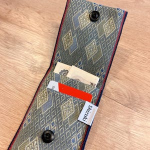 May include: Open fabric wallet with a geometric pattern in shades of blue, green, and gold. The wallet is open, revealing a red card and a small piece of paper. The brand name "Shizuki" is printed on a white tag.