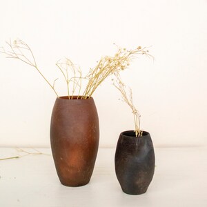 May include: Two ceramic vases, one brown and one black, with dried flowers in them. The vases are both oval shaped and have a rustic, handmade look.