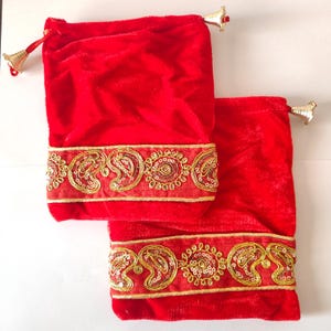 Könnte beinhalten: Zwei rote Samtbeutel mit goldenen Verzierungen und aufwendigen Stickereien. Die Beutel haben an jeder Seite einen goldenen Quasten.