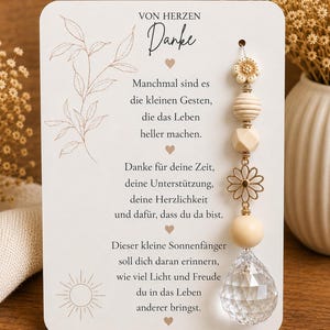Könnte beinhalten: Eine weiße rechteckige Karte mit dem Text "VON HERZEN Danke" und einem Gedicht, verziert mit einer Strichzeichnung von Blatt und Sonne. Rechts ist ein vertikaler Anhänger mit einer weißen Blume, Holzperlen, einer goldenen Margerite und einem Kristall.